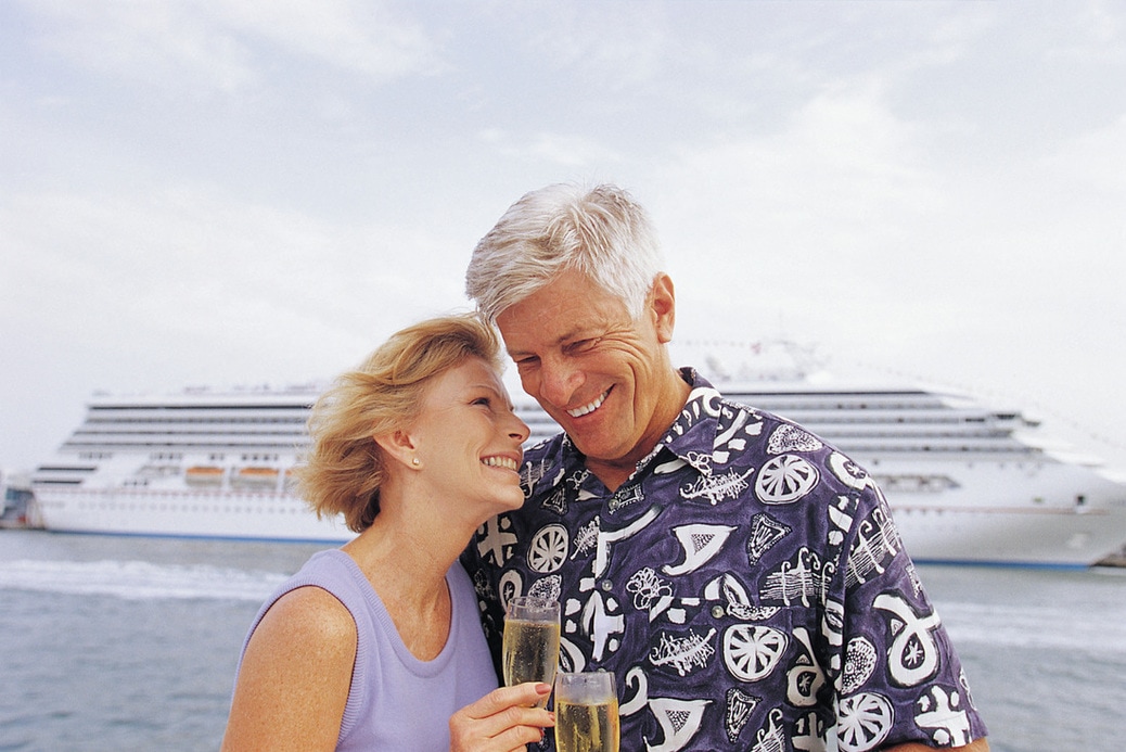 Old Caucasian couple toasting champagne in front of a cruise ship